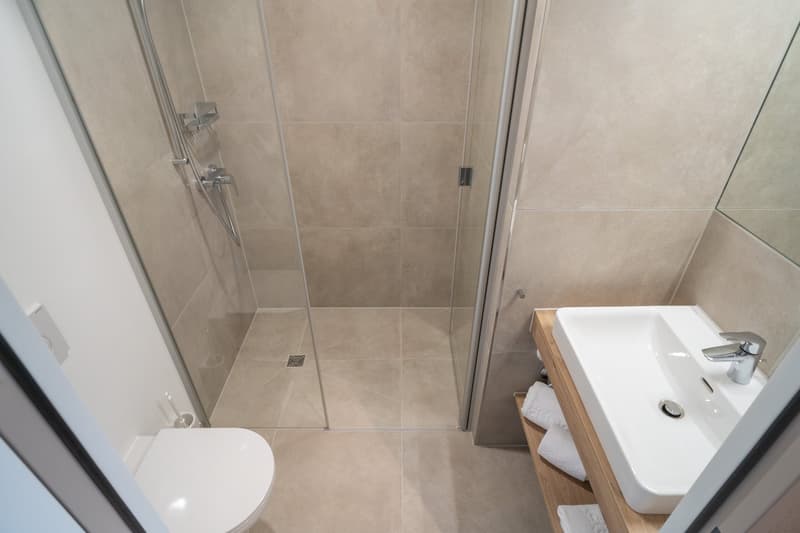 Tiled bathroom with a glass shower enclosure, a toilet, and a vanity with a sink and storage cabinet.