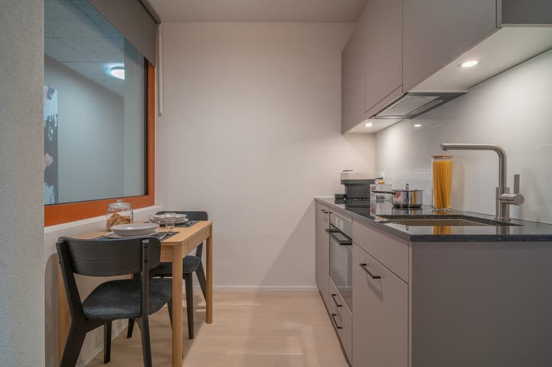 Modern kitchen with gray cabinets, black countertop, built-in dishwasher, and a small dining table with two chairs