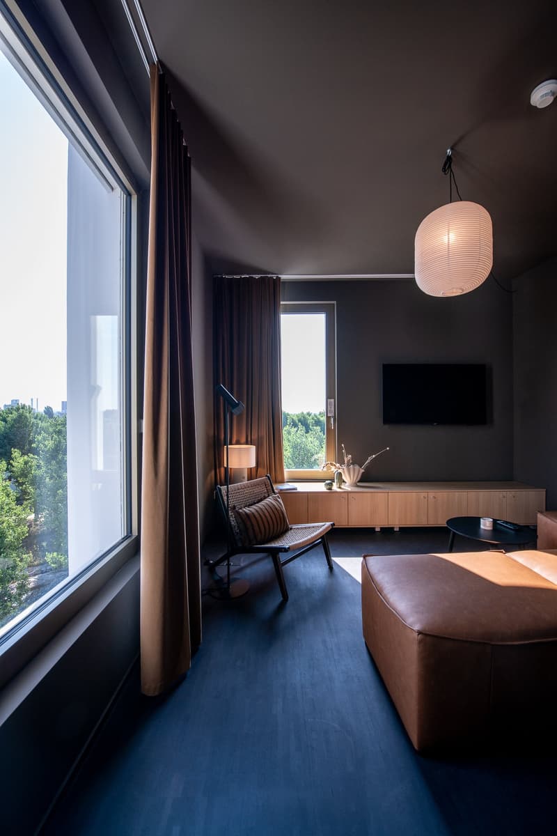 Large windows with a view, dark walls, wooden furniture, leather armchair, TV stand, and a hanging paper lantern light fixture.