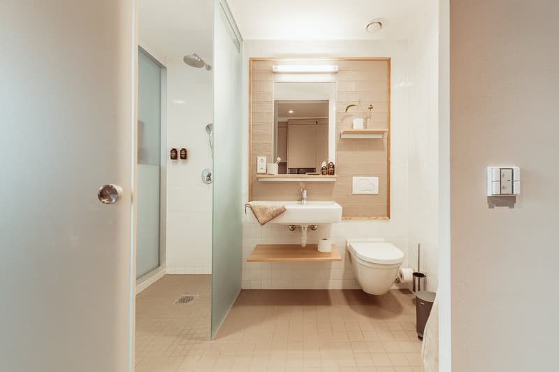 Modern bathroom with white tiles, wooden vanity, sink, toilet, and glass shower enclosure