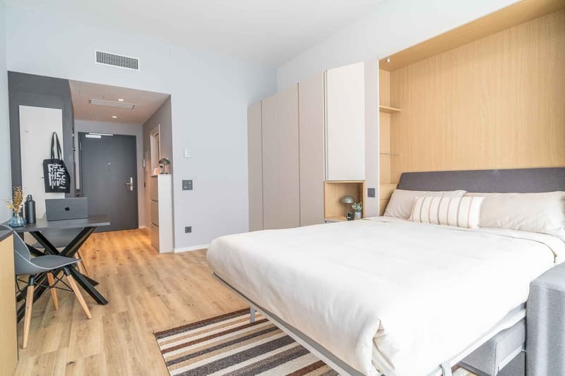 a room with a bed, desk, and chairs