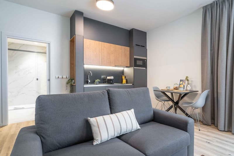 modern living room with gray sofa, wooden floor, open kitchen, dining table, microwave, sink, faucet, and shower