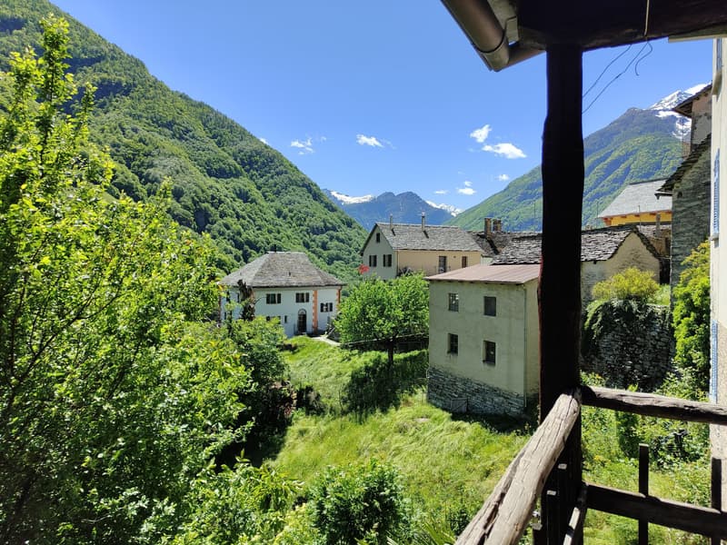 Talabwärts liegen schöne Dorfhäuser und hohe Bergspitzen im Blick. / A valle si vedono splendide case di paese e alte cime montuose