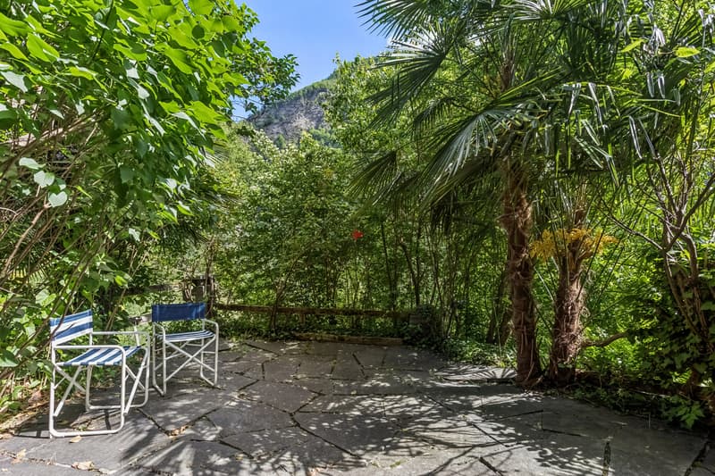 Auf dem Sitzplatz vor dem Haus ist man von Grün umgeben. / Nel posto a sedere davanti alla casa si è circondati dal verde
