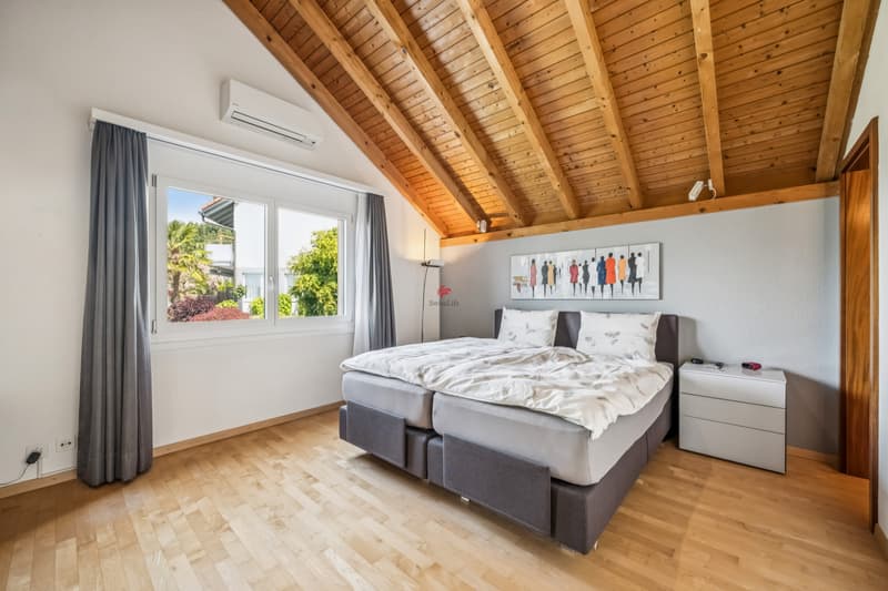 Schlafzimmer mit grosszügigem Fenster und Bad en suite. / a modern bedroom with wooden ceilings, hardwood floors, and a large window