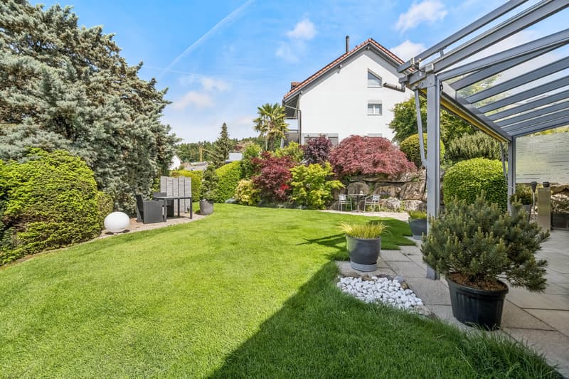 Weitläufiger Rasen und Pflanzen im Vorgarten. / the backyard of a home with a well maintained lawn and plants in the front yard