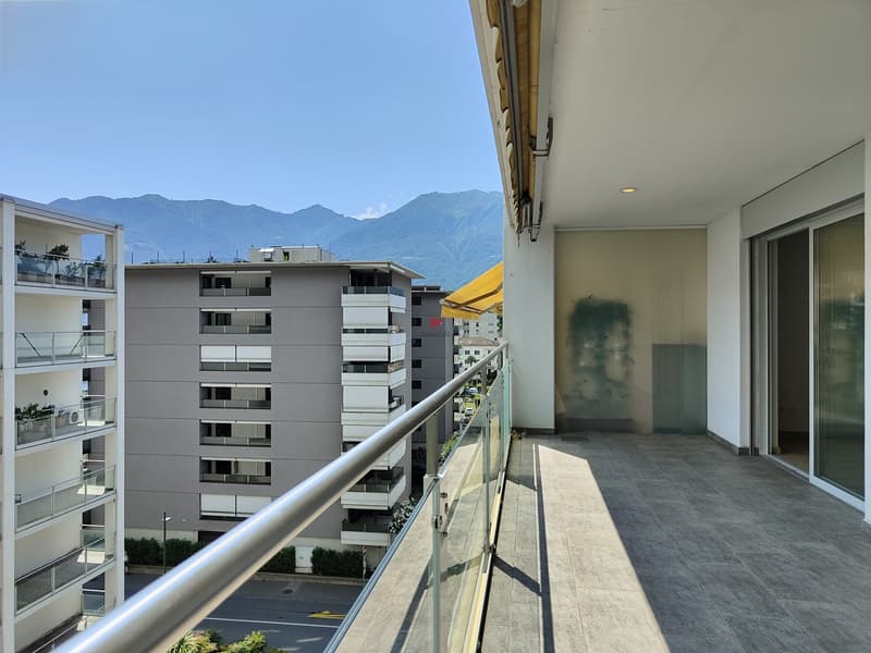 Raffinierte überdachte Terrasse mit dunklem Plattenboden und Blick in die Ferne, ideal für entspannende Momente an der frischen Luft. Der Blick von der Terrasse schweift über mehrere Berggipfel, un