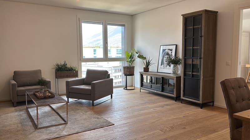 Spacious living room with large windows, hardwood floors, gray armchairs, wooden console table, and decorative plants
