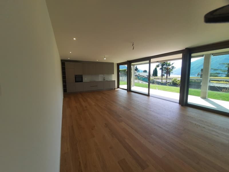 Spacious open-plan living area with hardwood flooring, large windows providing a scenic view of the outdoor landscape, and a modern kitchen with built-in cabinets and appliances.