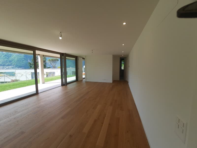 Spacious living room with large windows overlooking a garden, hardwood flooring, and recessed lighting.