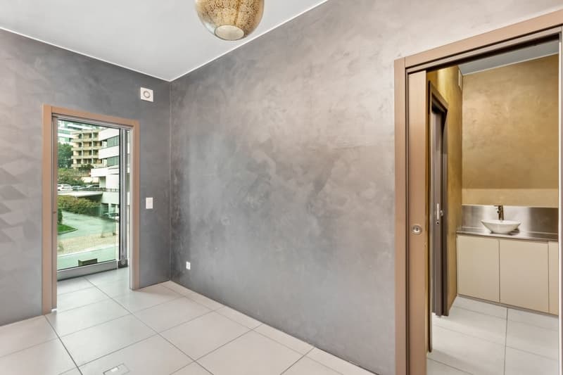 Modern room with gray walls, white tiled floor, glass door, white sink with faucet, and light fixture