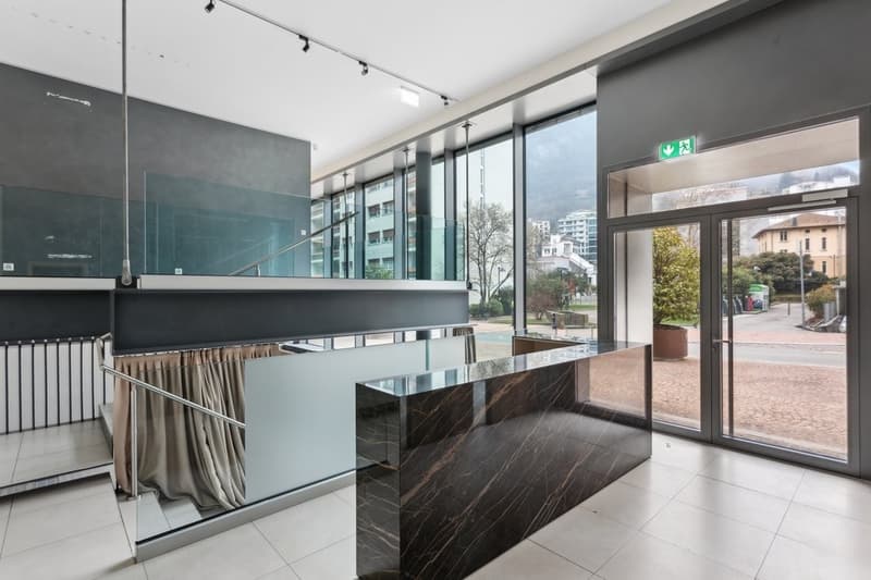 Modern foyer with marble countertop, glass wall, large windows, open staircase, white tiled floor