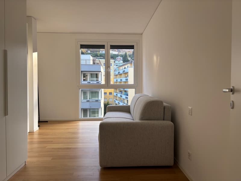 white walls, wooden floor, large glass window with view, gray sofa