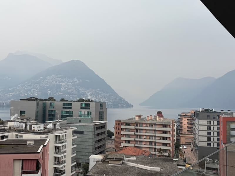 Urban city view, high rise buildings, mountains in the distance, and a body of water.