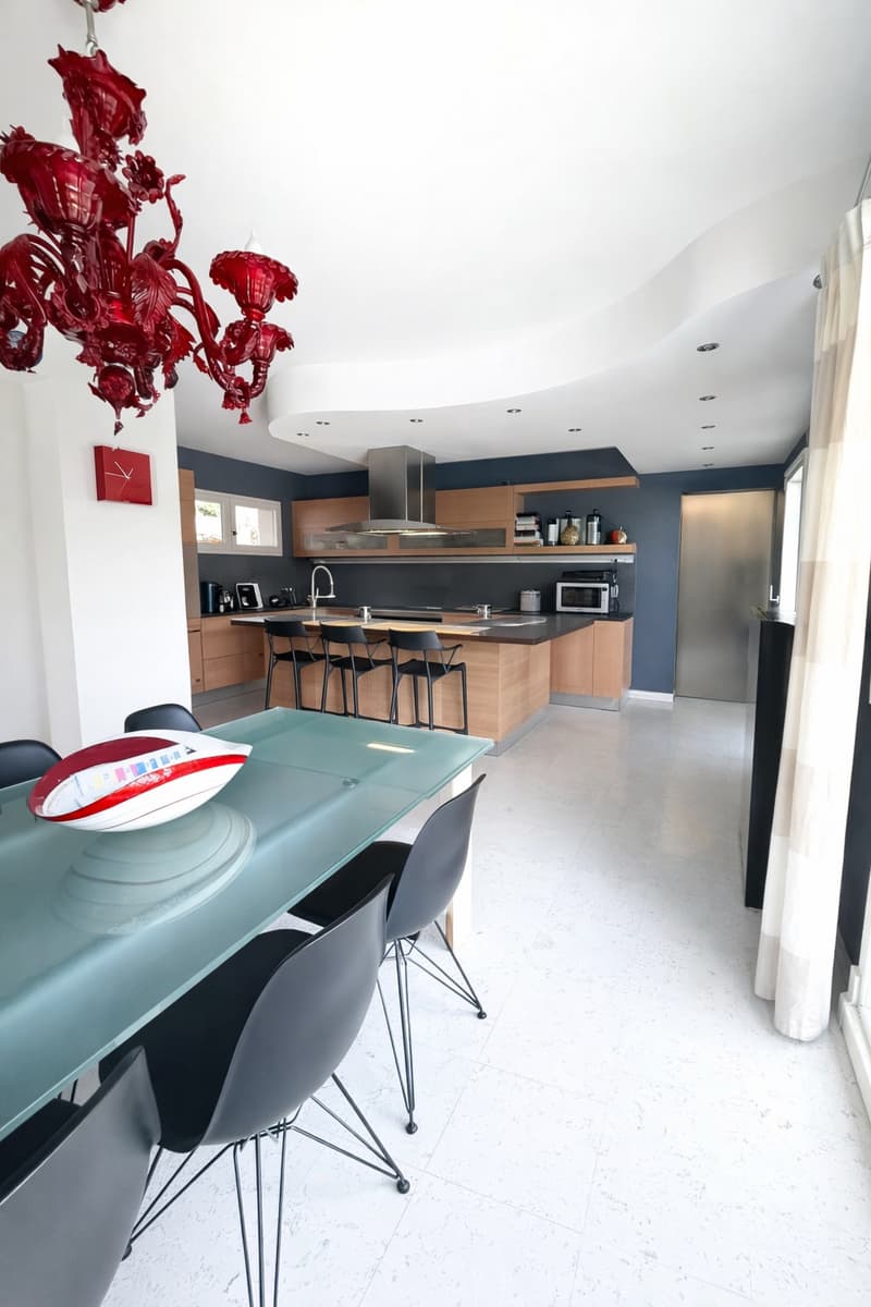 modern kitchen with dining area, glass table, black chairs, red chandelier, wooden cabinets, white floor