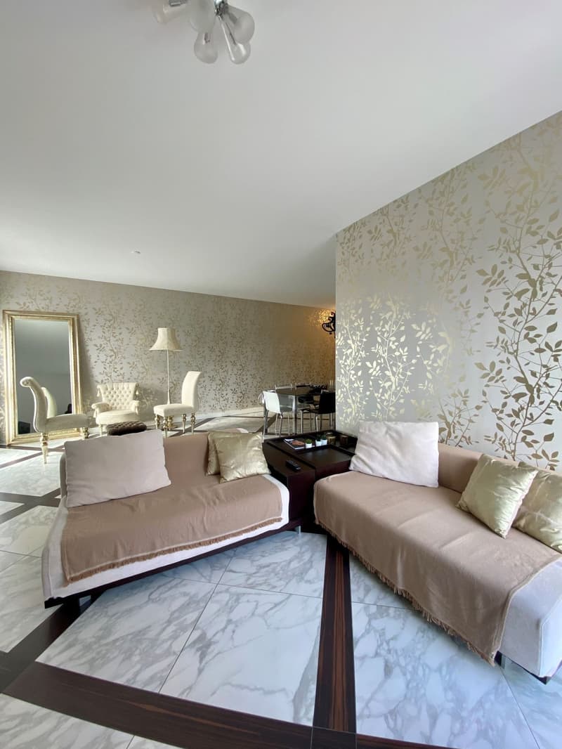 Living room: large L-shaped sofa, golden wall covering, marble flooring, chandelier, mirror, side table, lamps, chairs, dining table and chairs.