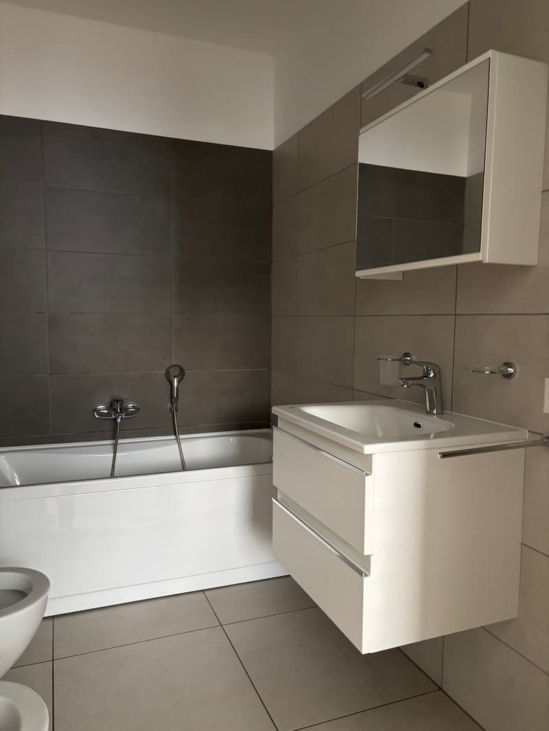 modern bathroom with white bathtub, sink, modern toilet and cabinet, mirror and lighting