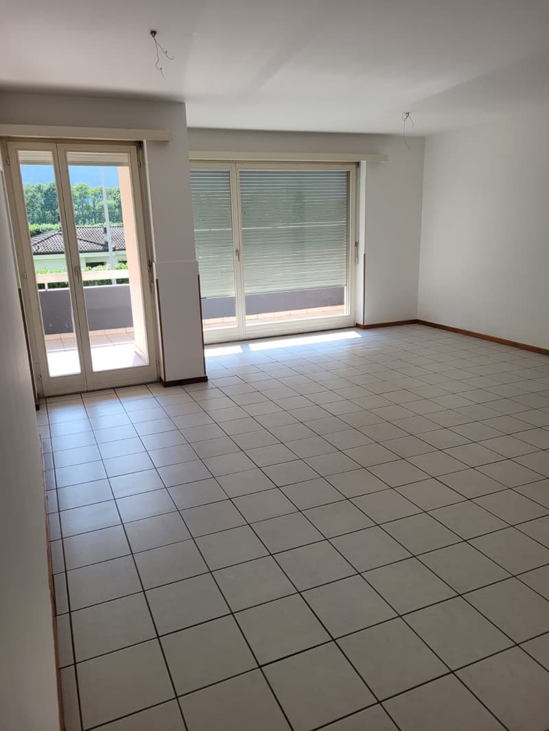 Spacious living room with large windows, sliding glass doors leading to a balcony, and tile flooring.