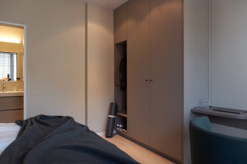 Bedroom with bed, bedsheet, and a wooden floor, large walk-in closet, a desk with a chair, and a modern office space.