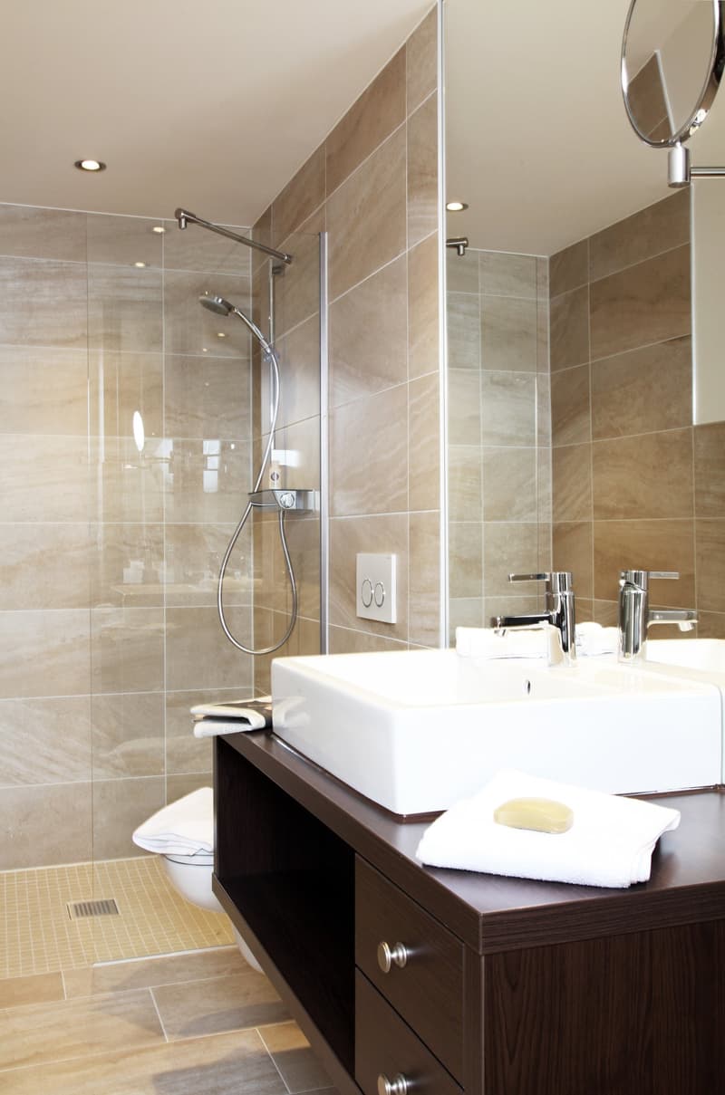 Modern bathroom with beige tile walls, glass shower enclosure, vanity with sink, and a dishwasher unit.