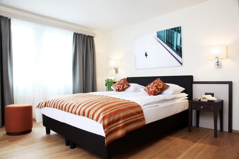 Spacious bedroom with large windows, hardwood floor, black bed frame, striped bedding, side table, and wall art