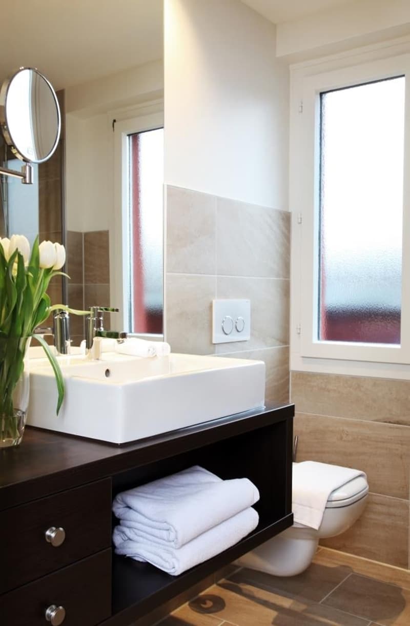 Modern bathroom with white walls, vessel sink, dark wood vanity, and towels stored in the vanity cabinet