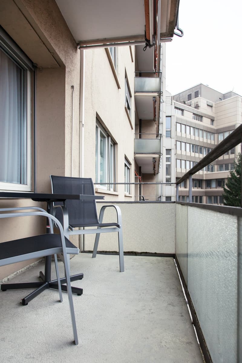 Small balcony with a desk and chair, overlooking a residential building