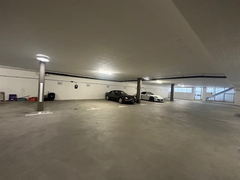 Large indoor parking garage with concrete floor, several parked cars, and overhead lighting.