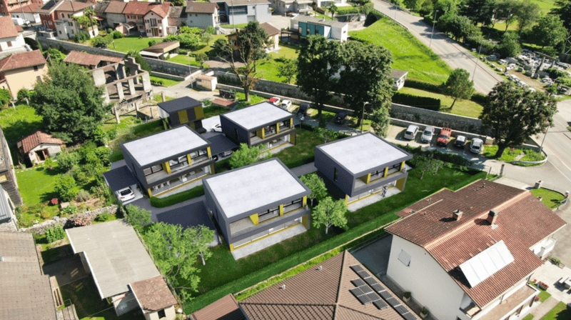 Aerial view of a residential complex with several modern, multi-story buildings surrounded by lush greenery and a parking area.