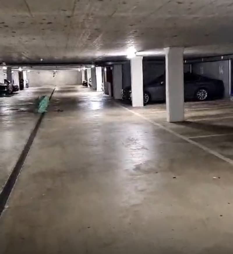 underground parking lot, with 2 cars parked, multiple white pillars, lights on ceiling