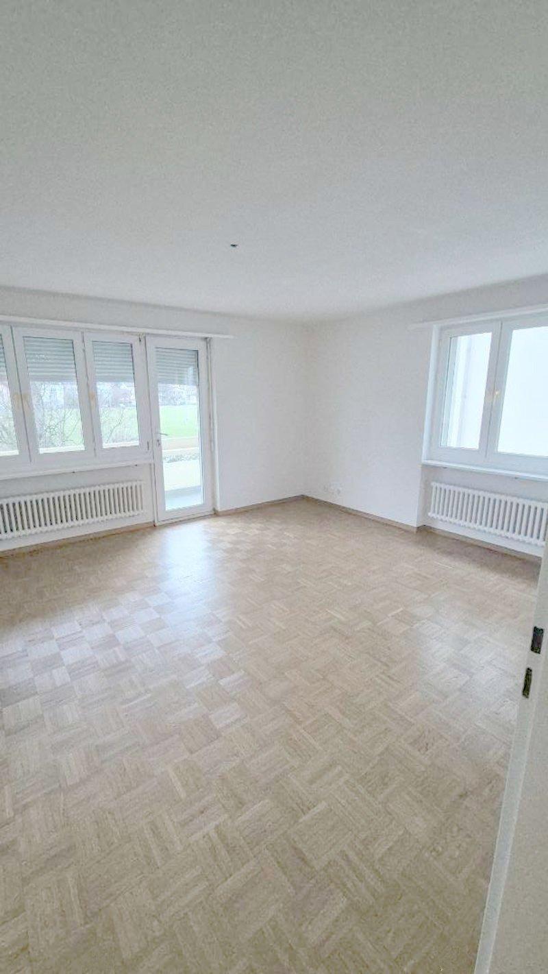 open room, wooden parquet floor, white walls, sliding glass door, two windows, white radiators