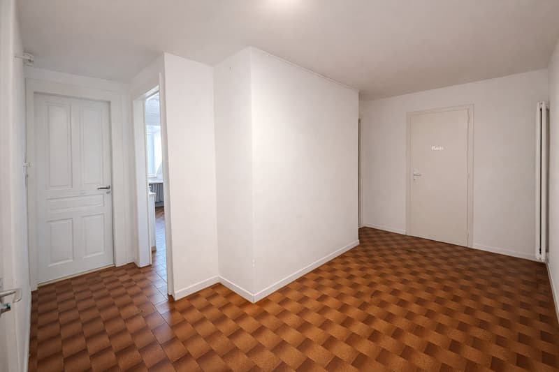 Empty room with white walls, brown checkered flooring, two doors, one leading to another room
