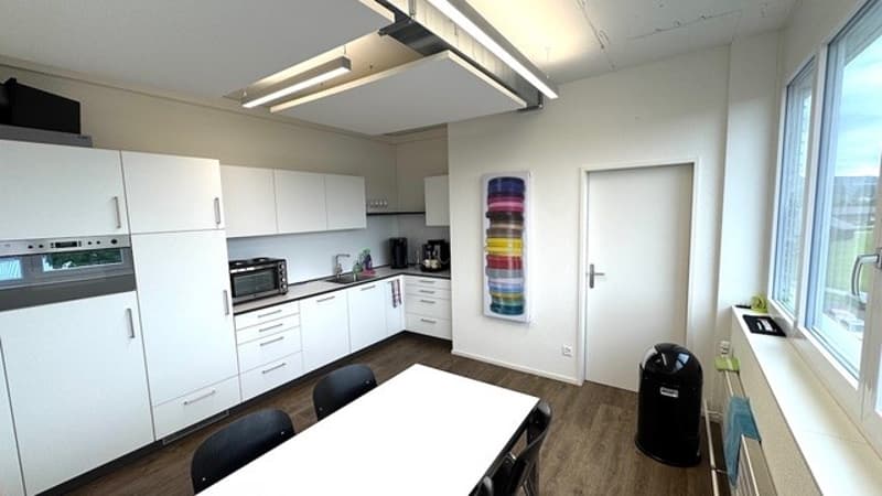 modern kitchen with white cabinets, wooden floor, white table, black chairs, microwave, sink, refrigerator, oven, trash bin, radiator