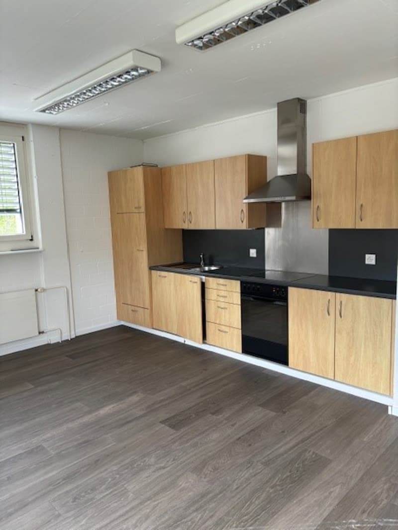 Spacious kitchen with wooden cabinets, black countertops, stainless steel appliances including a dishwasher, and hardwood-style flooring.