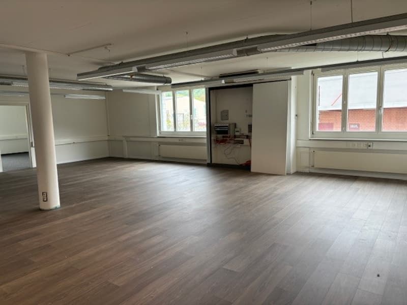 Large open-plan office space with hardwood flooring, white walls, and exposed ceiling beams. The space appears to be a commercial or industrial setting, potentially suitable for use as an office, studio, or workshop.