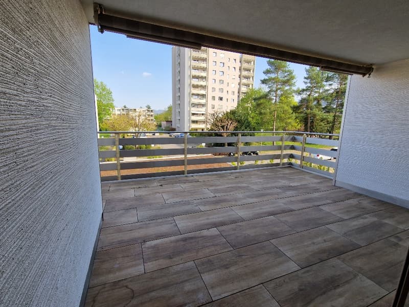 empty balcony with wooden floor, metal railing, view of trees and buildings