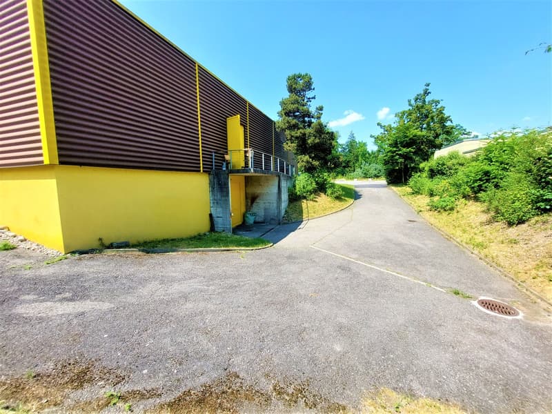 Industrial building with yellow and brown exterior, small side road, trash bin, and drainage