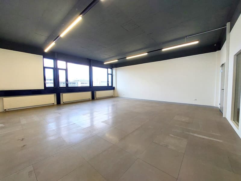 Empty room with white walls, tiled floor, large windows, and ceiling lights