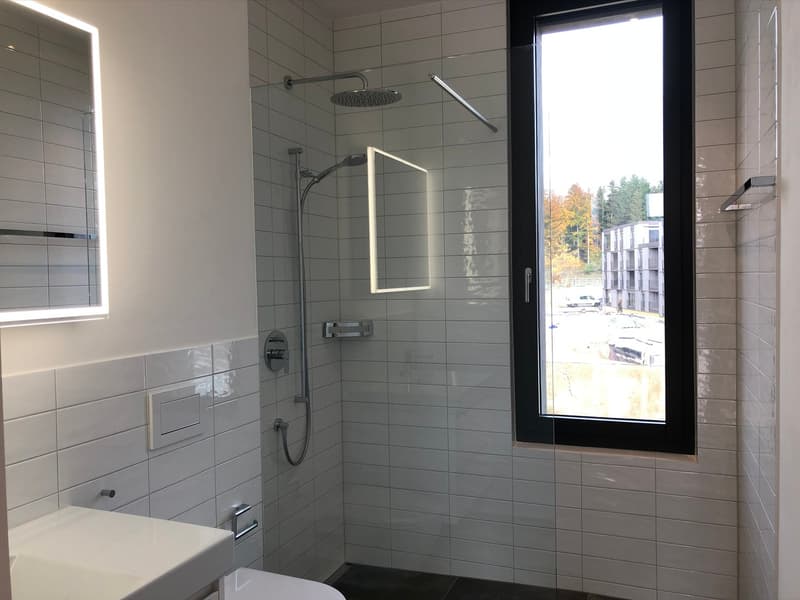 modern bathroom with white tiles, glass shower enclosure, shower head, sink, toilet, mirror, window