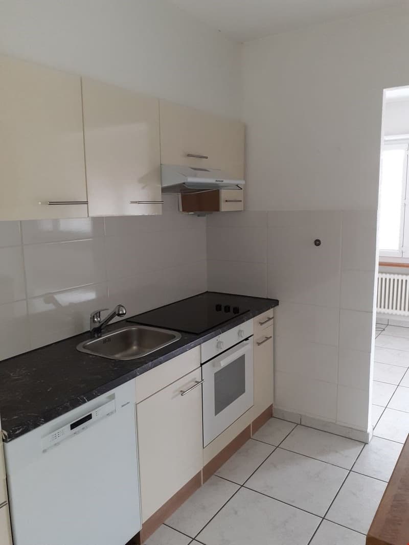 modern kitchen, black countertop, stainless steel sink, built-in oven, dishwasher, washing machine, white tiled walls