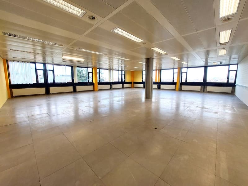 large open space, tiled floor, fluorescent ceiling lights, large windows, yellow pillars
