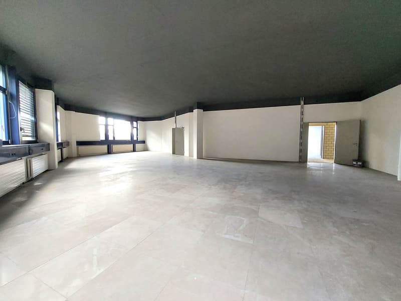 Empty room with white tiled floor, white walls, gray ceiling, windows, and two doors.