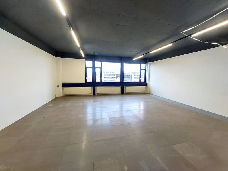 Empty room with white walls, tiled floor, large windows, and ceiling lights