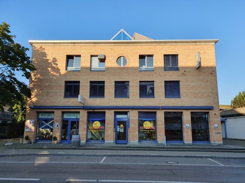 3 story building, blue trim, round windows, commercial windows, 3 entrances, barrel outside, plants