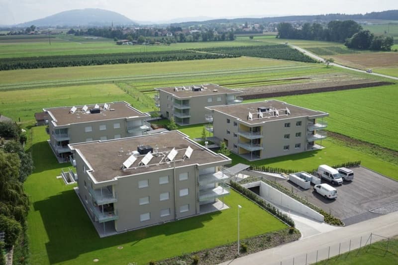 Three apartment buildings, green lawn, parking lot, solar panels on the roofs