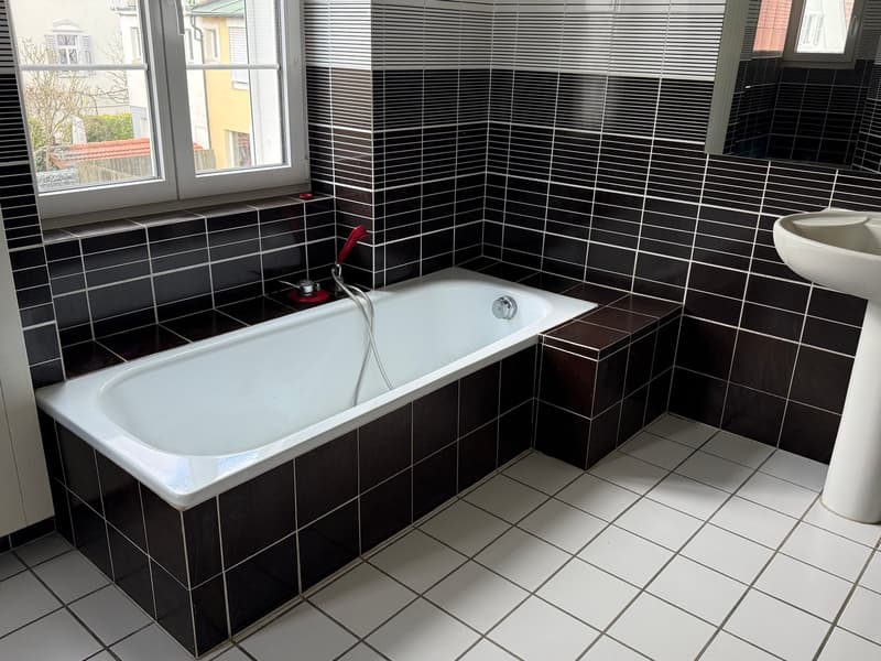 Bathroom with white bathtub, black and white tiles, white sink, window with blinds