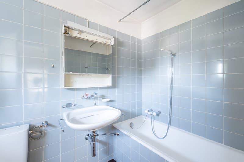 Bathroom with blue tiles, white sink, bathtub, shower, mirror, and toilet