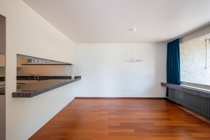 empty room, wooden floor, white walls, kitchen counter, sink, faucet, window with blue curtain, radiator