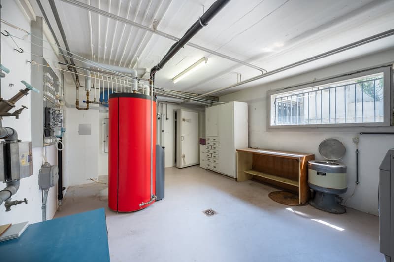 Utility room with a red water heater, white cabinets, a wooden desk, and a window with bars.