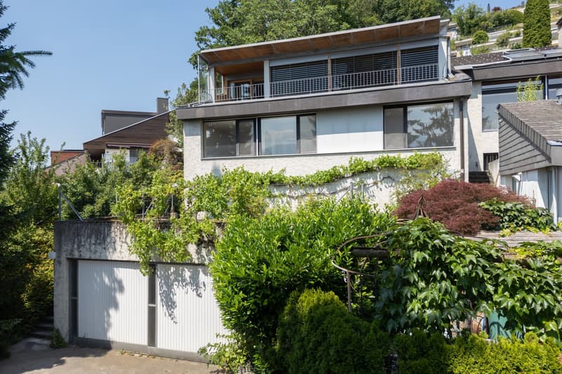 modern house, white exterior, large windows, balcony, garage, surrounded by greenery